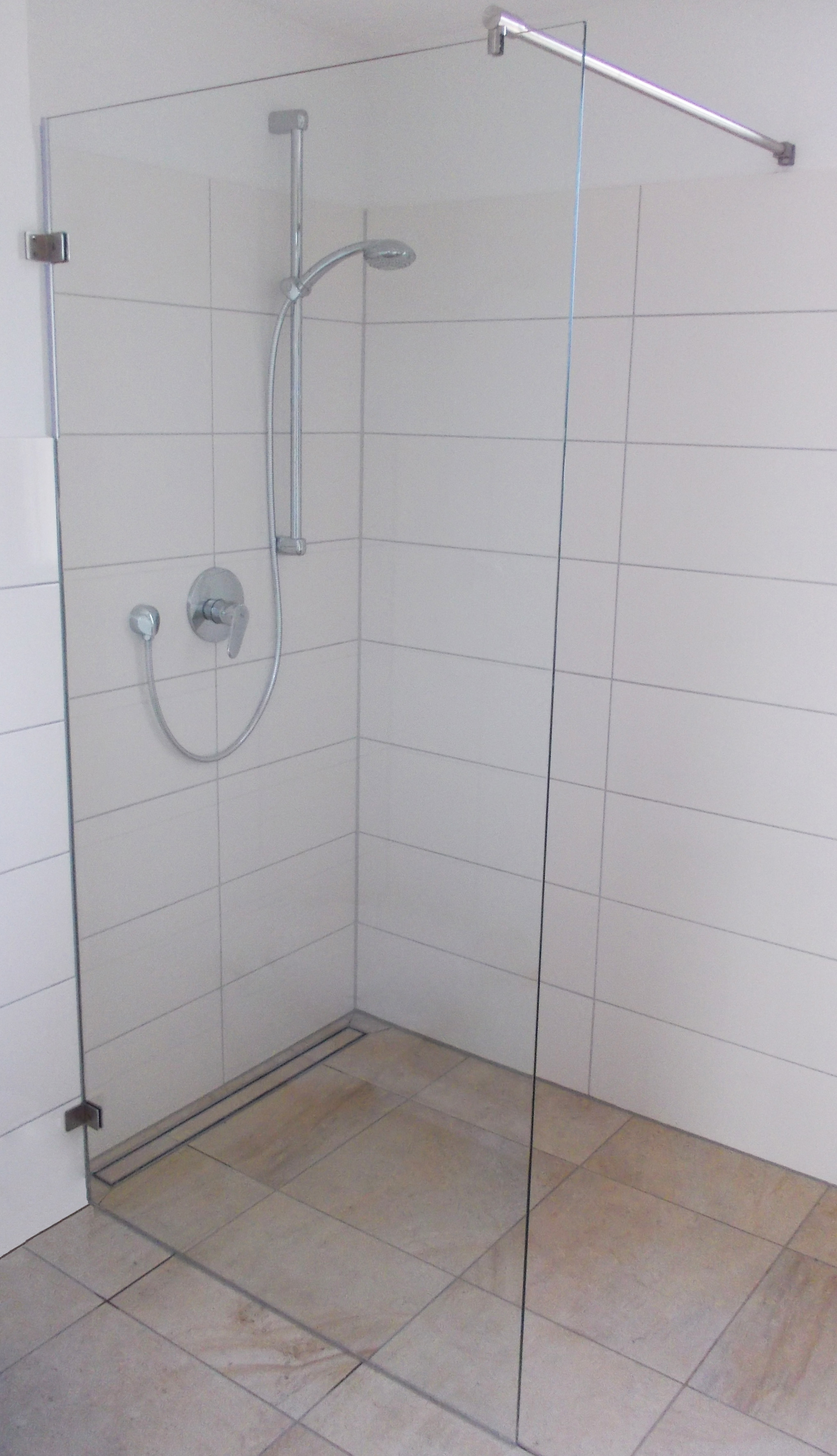 Actual zero-threshold walk-in shower with seamless tile floor, linear trench drain, and frameless glass screen.